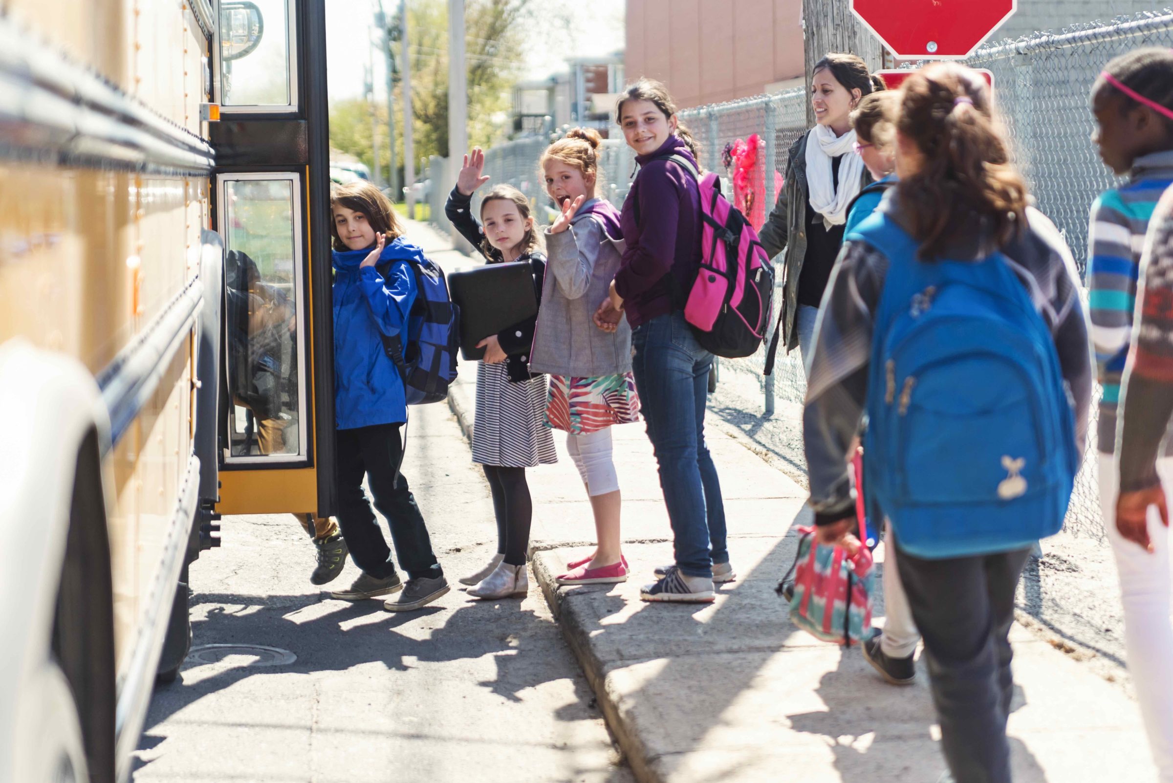 Kids in line waiting to get on school bus saying goodbye.