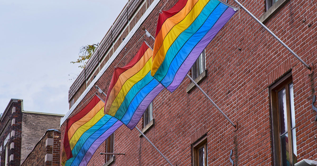 Trois drapeaux de la fierté accrochés à une édifice dans le quartier gai de Montréal.