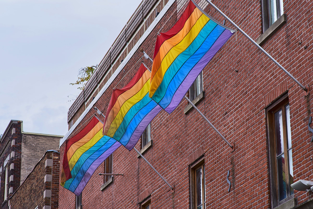 Trois drapeaux de la fierté accrochés à une édifice dans le quartier gai de Montréal.