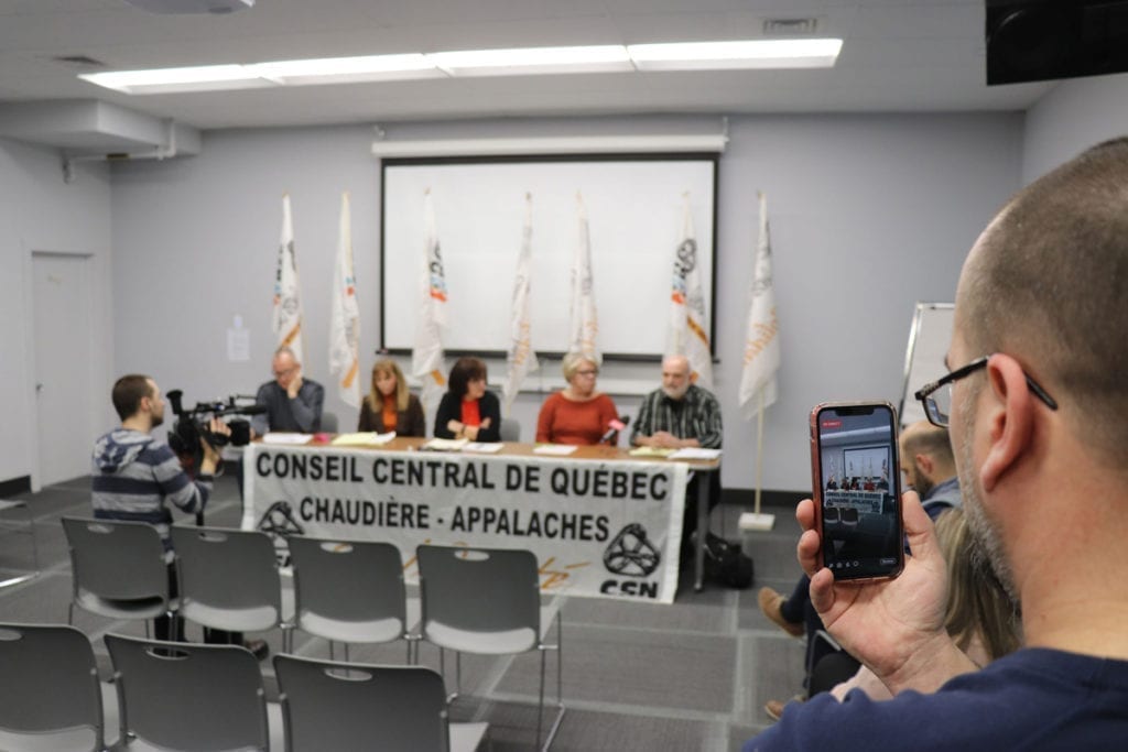 Photo de conférence de presse au CCQCA, 5 personnes à une table, une personne qui filme sur son cellulaire