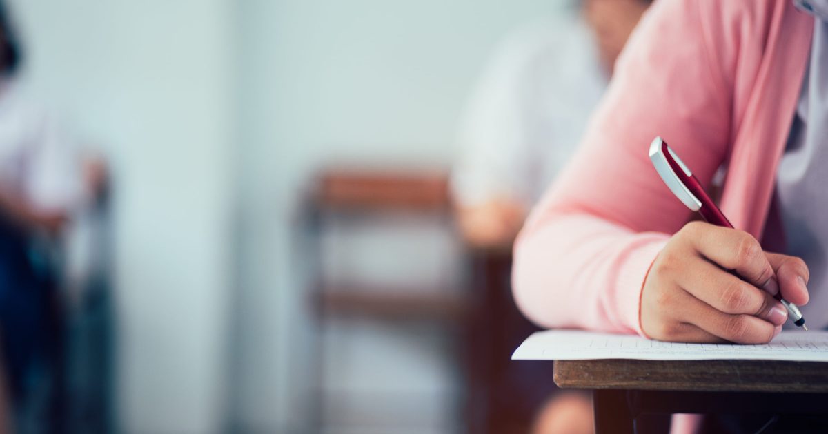 Hand of students writing and taking exam with stress in classroom