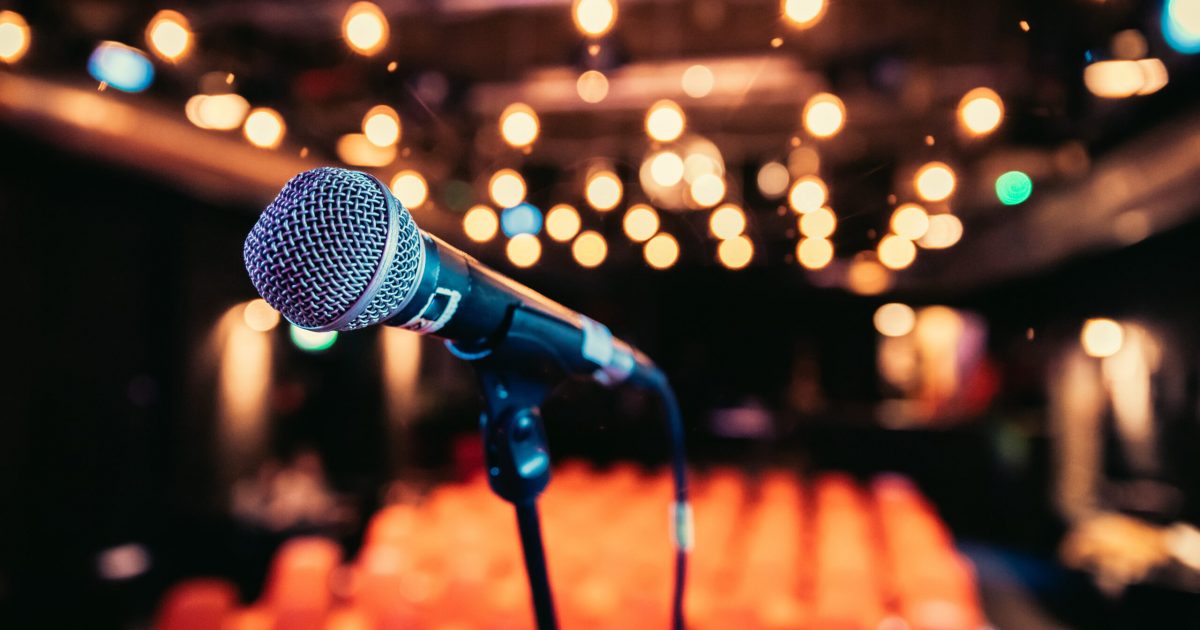 Empty event hall: Close up of microphone stand, empty seats in the blurry background