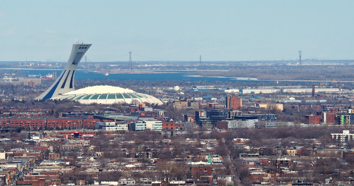 Olympic Stadium (Stade Olympique) protruding the Montreal skyline on a cold winter day.  In this picture, the skies are clear, by the river is partially frozen along the shore.