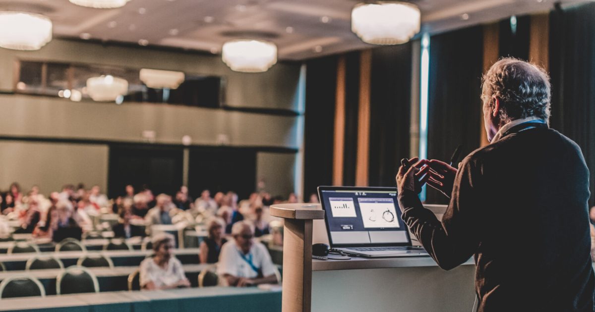 Senior public speaker giving talk at scientific conference.