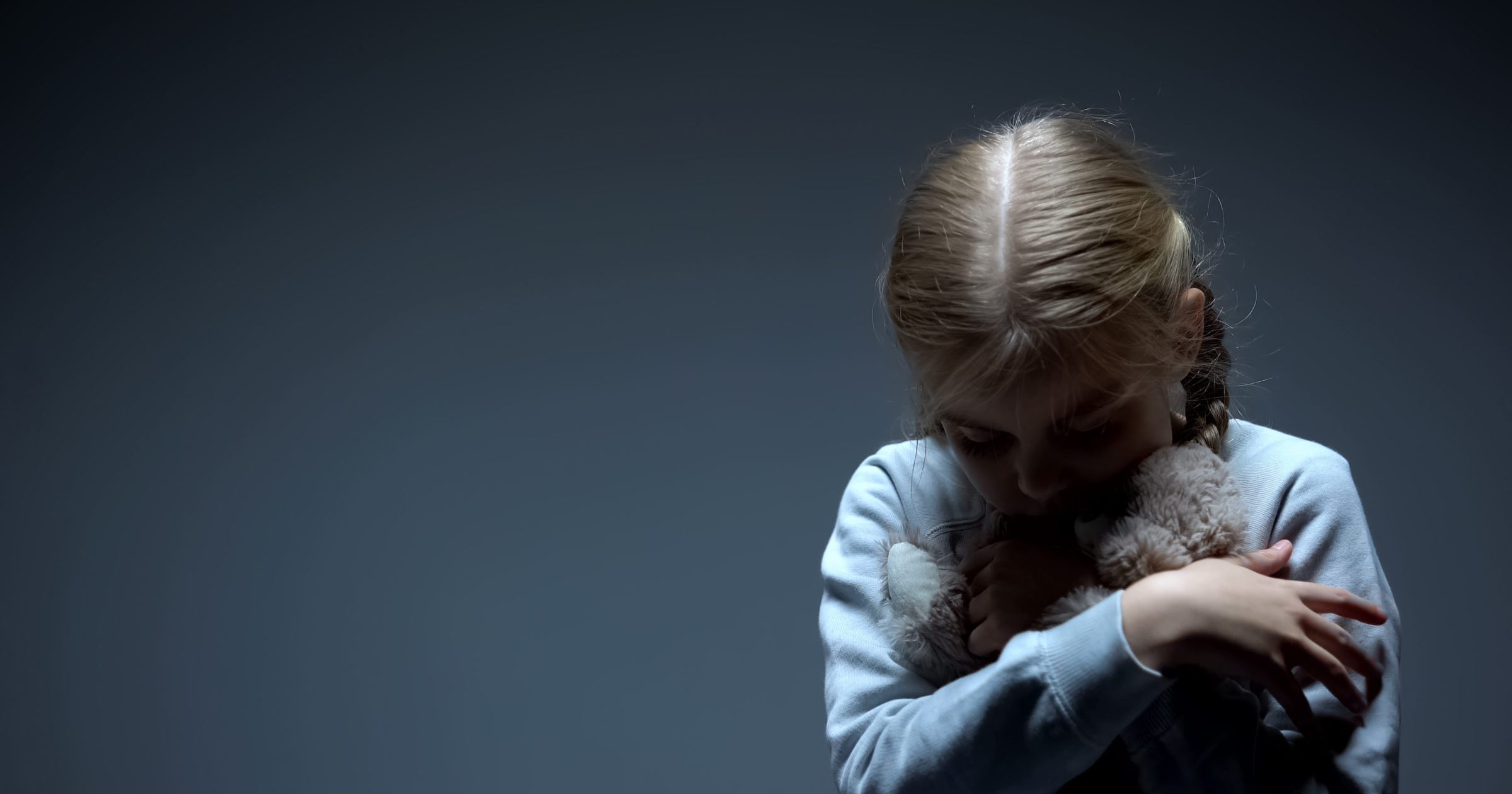 Lonely little child hugging teddy bear, bullying concept, dark background